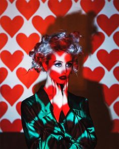 a woman with her hands on her face standing in front of a heart - shaped wall