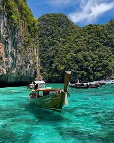 several boats floating on the water in front of some mountains and cliffs, with clear blue water