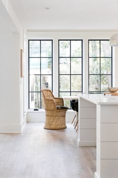 a kitchen with white walls and wooden floors has large windows that look out onto the backyard