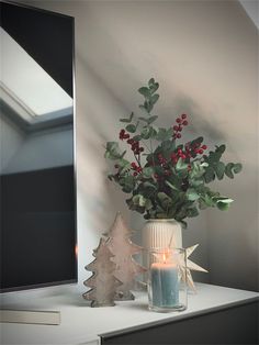 a vase filled with greenery sitting on top of a white table next to a mirror