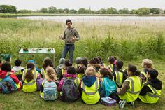 a man standing in front of a group of children sitting on the ground next to each other