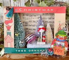 an old fashioned christmas frame with ornaments and trees in it on a table next to sheet music