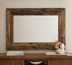 a wooden mirror sitting on top of a table next to a vase with flowers in it