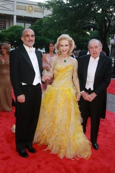 two men and a woman in formal wear standing on a red carpet at an event