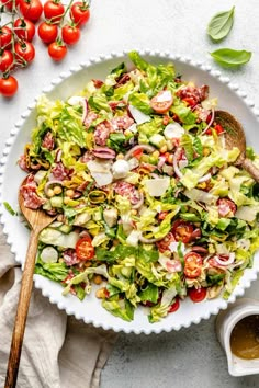 a salad with tomatoes and lettuce in a white bowl next to a wooden spoon