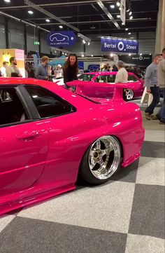 the pink car is parked on the checkered floor in front of other people at an auto show