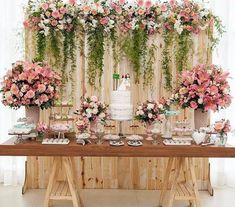 a table topped with lots of pink and white flowers next to a wall covered in greenery