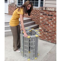 a woman is bending over to pick up something out of the trash can that's in front of her house