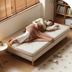 a woman laying on top of a bed next to a table with a book shelf