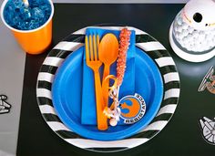 a blue and black plate with orange plastic utensils on it next to an orange cup