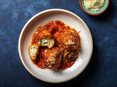 a white plate topped with meat covered in marinara sauce next to a bowl of cheese