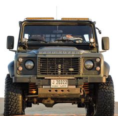 the front end of an army truck with its lights on, parked in a parking lot