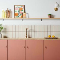 a kitchen with pink cabinets and white tiled walls, potted plants on the shelf