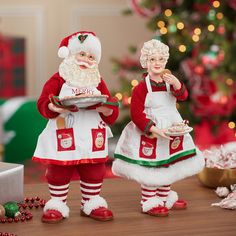 two figurines dressed as santa clause and mrs claus holding a tray with food on it