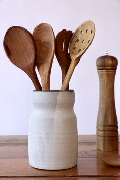 several wooden spoons and spatulas in a white ceramic cup on a table