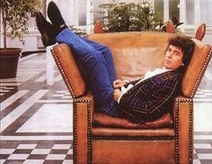 a man laying on top of a brown chair in a room with black and white checkered flooring