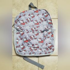 a hello kitty backpack sitting on the floor next to a tile wall with a gray strap