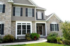 a large house with lots of windows and plants in the front yard, on a sunny day