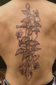 the back of a woman's lower back tattoo with flowers and swords on it