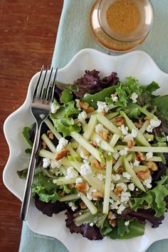 a salad with lettuce, feta cheese and nuts in a white bowl