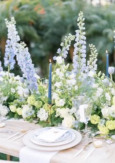 the table is set with blue and white flowers, candles, and plates on it