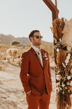 a man in an orange suit standing next to a wooden cross with flowers on it