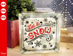 a glass block with the words let it snow in red and black lettering on it