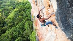 a man climbing up the side of a cliff with his hands in the air while holding onto a rope