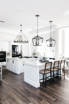 a large kitchen with white cabinets and wood flooring is pictured in this image, there are several lights hanging over the island