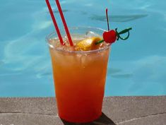 an orange drink with two straws and a cherry garnish sits next to a swimming pool