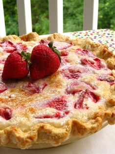 a strawberry pie with two strawberries on top sitting on a table in front of a window