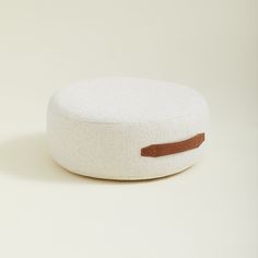 a white round cushion with a brown leather patch on the front and back side, sitting on a plain surface