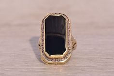 This stunning piece, known as The Art Deco Elegance, features a captivating elongated emerald cut onyx tablet at its center. The rectangular cut onyx is elegantly bezel set in 14 karat yellow gold, designed with intricate filigree detailing that adds a touch of vintage sophistication which continues down the shank. The ring is crafted in 14 karat yellow gold and is currently a finger size 2.75. Art Deco Onyx Ring, Filigree Ring, Art Deco Era, Onyx Ring, Bezel Setting, Emerald Cut, Rings Statement, Statement Rings, Onyx