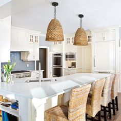 a large kitchen island with wicker chairs and lights hanging from it's ceiling