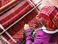 a woman is weaving fabric with two large wooden looms in front of her on the floor