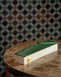 a small green and white building sitting on top of a wooden table in front of a patterned wall