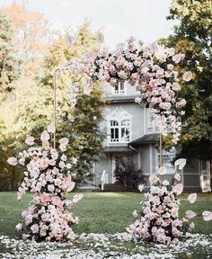 an arch made out of pink flowers in front of a house with white petals on the ground