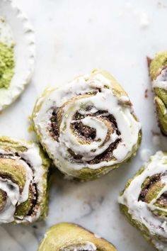 several pastries with white icing on top of a marble counter next to green powdered sugar