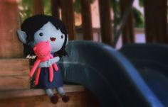 a stuffed doll holding a pink toy in her arms on a playground slide area with wooden railings