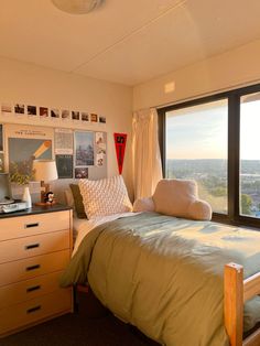 a bedroom with a bed, dresser and large window overlooking the cityscape in the distance