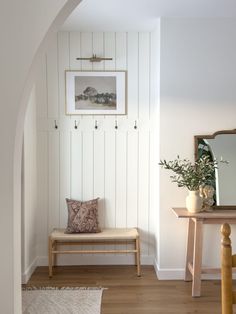 a room with a bench, mirror and vase on the wall next to a table