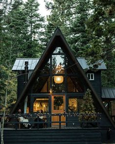 a - frame cabin in the woods with lights on it's porch and deck