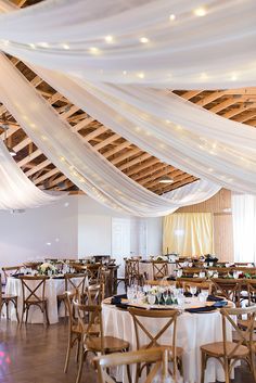 a room filled with lots of tables covered in white draping and wooden chairs