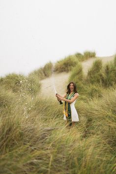 a woman standing in tall grass holding a wine bottle and sprinkles with water