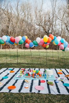 a table topped with lots of balloons and confetti on top of a black and white blanket