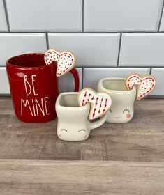 three ceramic mugs with hearts on them sitting next to a red mug that says be mine