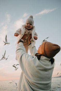 a man holding a baby up to the sky with seagulls flying around him