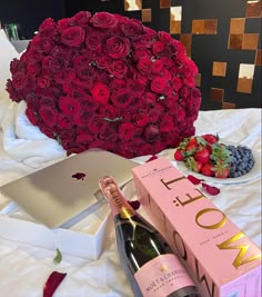 a bottle of wine and a box of strawberries on a bed next to a heart shaped rose