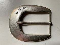 a metal belt buckle with small black dots on the front and sides, sitting on a white surface