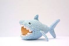 a crocheted toy shark with its mouth open and teeth wide open, on a white surface